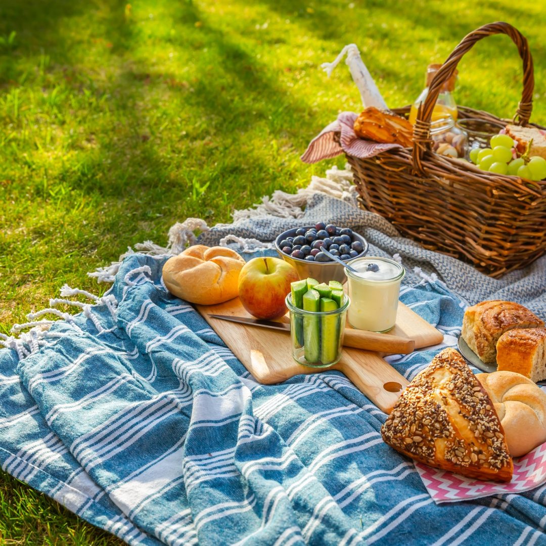 Picnic duvet and basket with different food, fruits, orange juice., yogurt and bread on green grass
