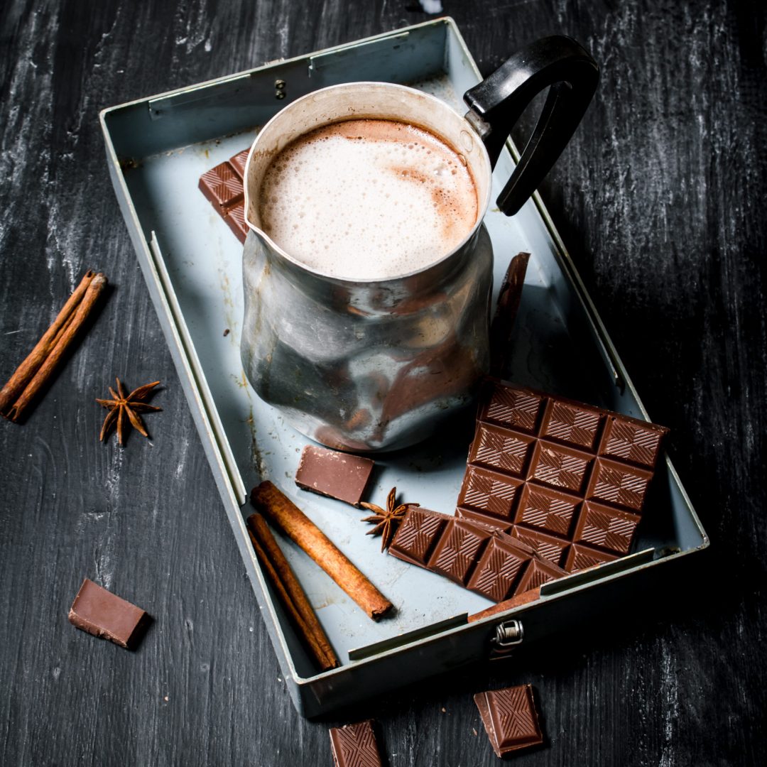 Hot chocolate with cinnamon and bitter chocolate. On black rustic background.