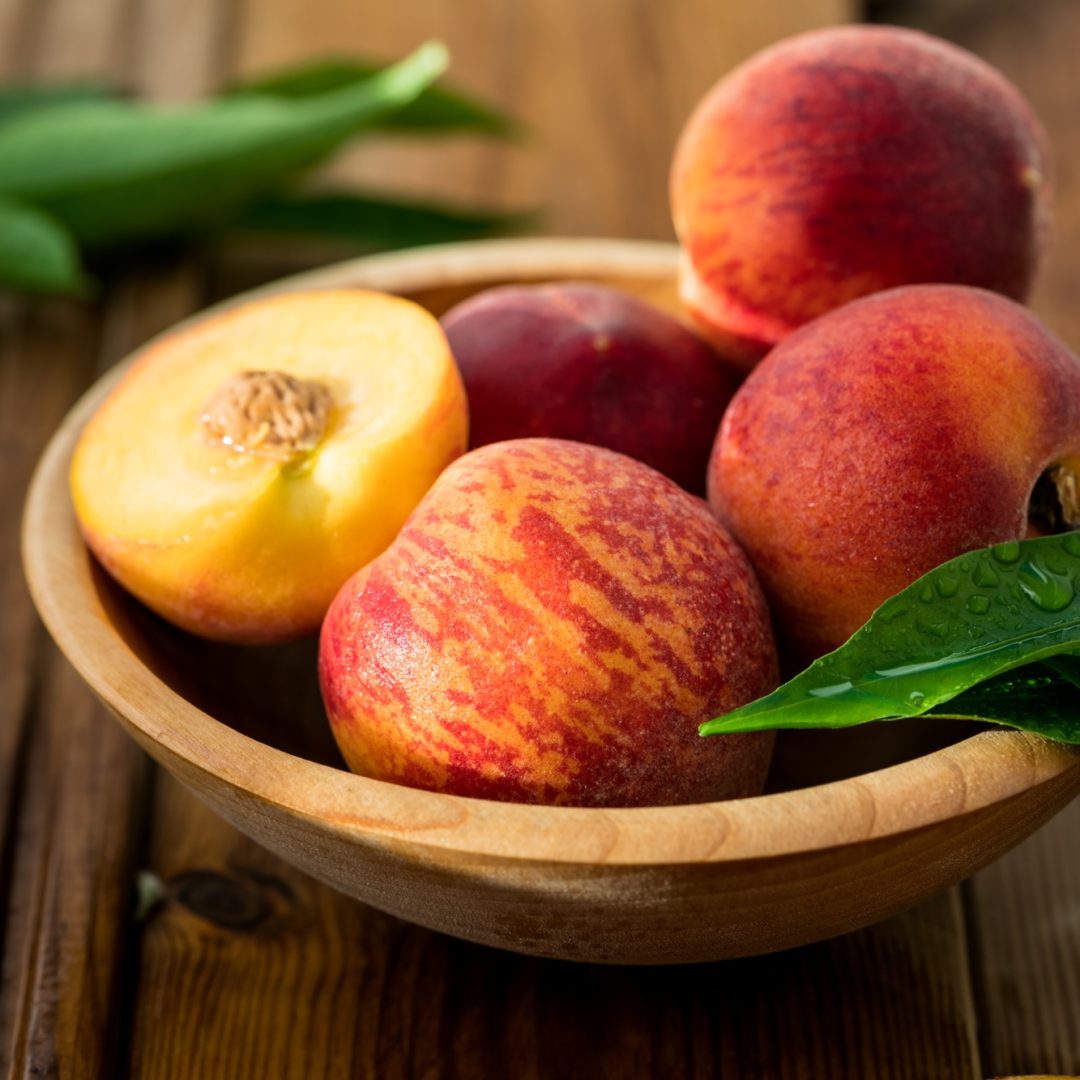 Peaches with leaves in a wooden bowl with peach in halves on top.juicy peaches. Harvest